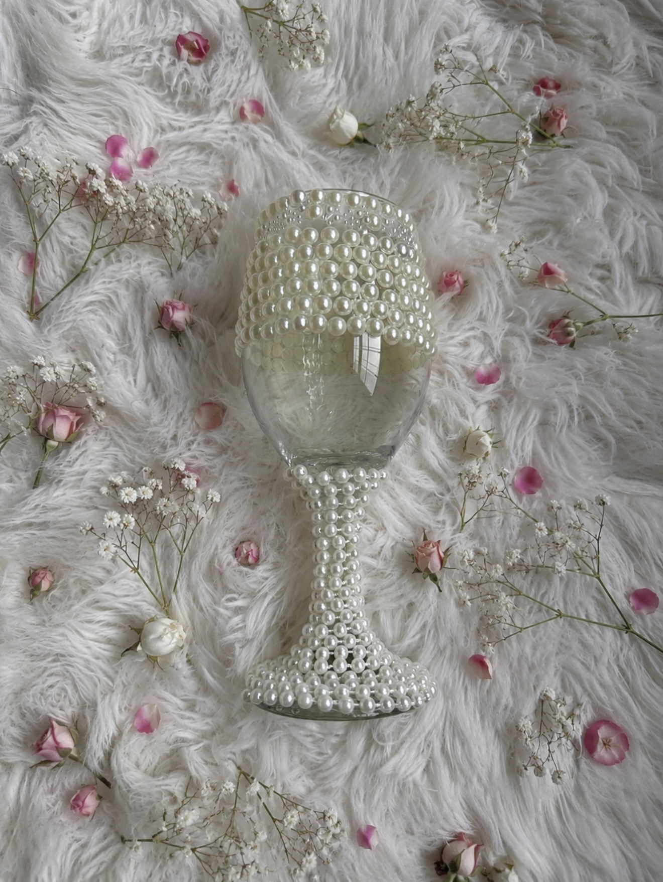 Glass goblet hand-decorated with ivory pearls, styled on white faux fur with pink rosebuds and baby's breath