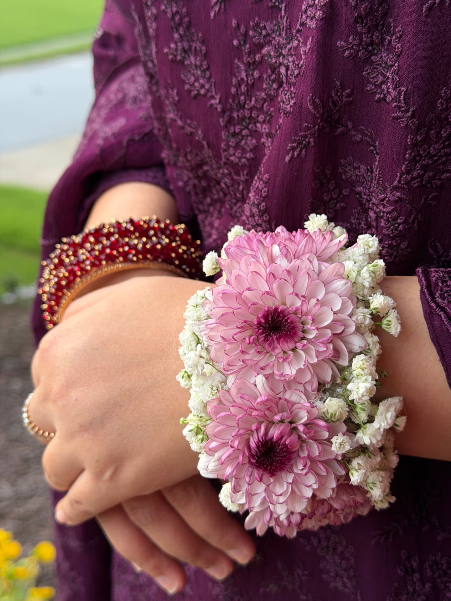 Close-up of a blush pink chrysanthemum and baby's breath floral cuff worn with a plum embroidered outfit