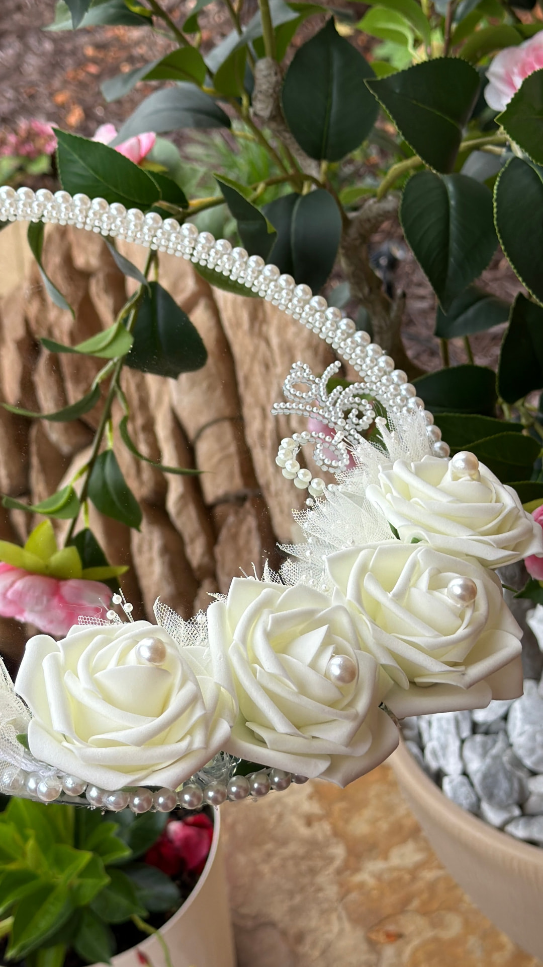 Bridal mirror trimmed with pearl beading, tulle and ivory roses photographed among green foliage and pink camellias