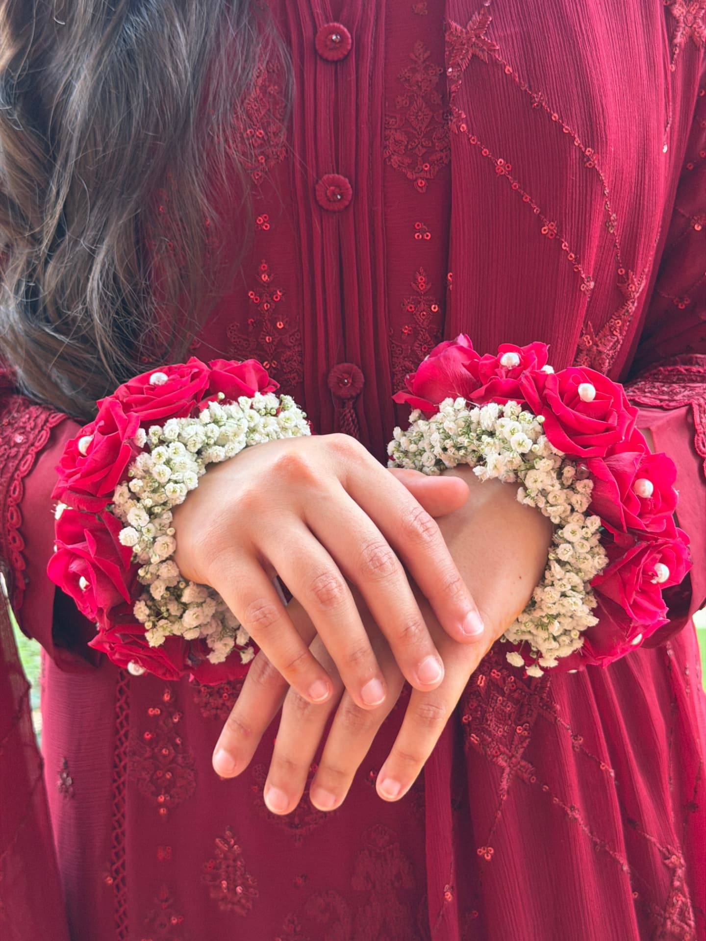 Pair of red rose and baby's breath floral bracelets with pearl centres worn over a maroon embroidered dress